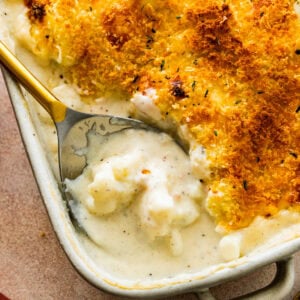 Spoon scooping creamy cheesy cauliflower casserole from a baking dish.