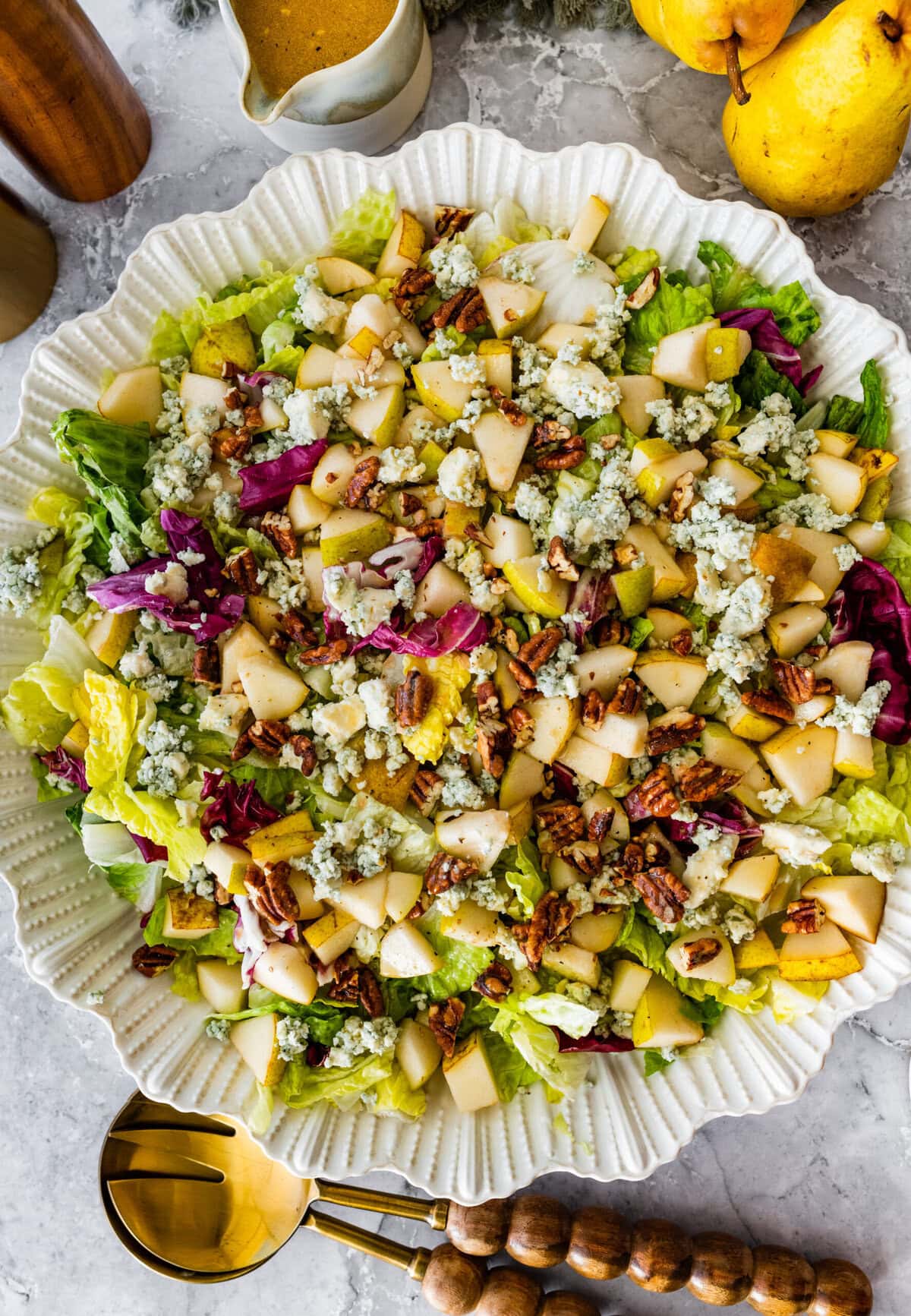 pear gorgonzola salad in a white serving bowl with salad servers near it.