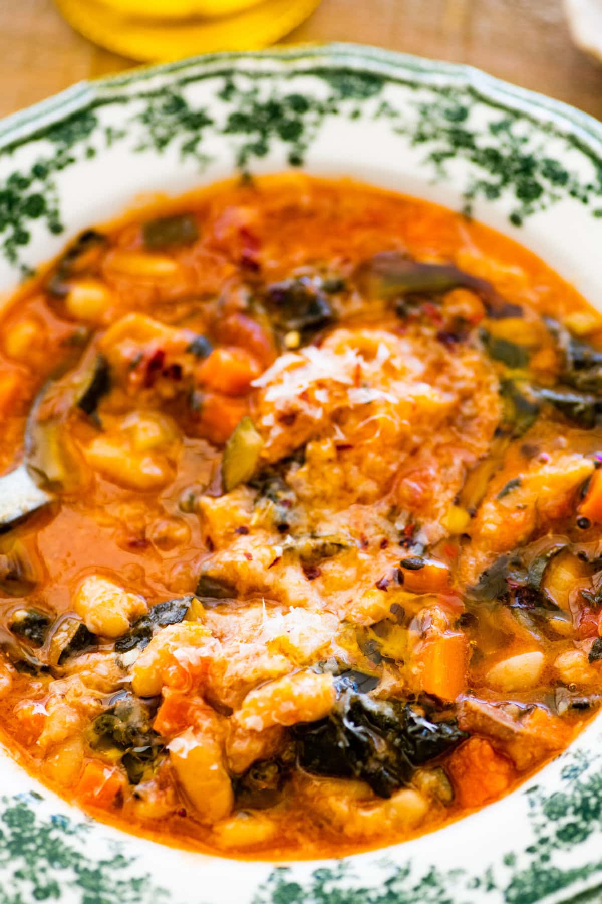 A warm bowl of the tuscan ribollita soup in an old fashioned bowl. Extra freshly grated parm on top for garnish. A spoon in the bowl.