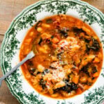 A warm bowl of the tuscan ribollita soup in an old fashioned bowl. Extra freshly grated parm on top for garnish. A spoon in the bowl.