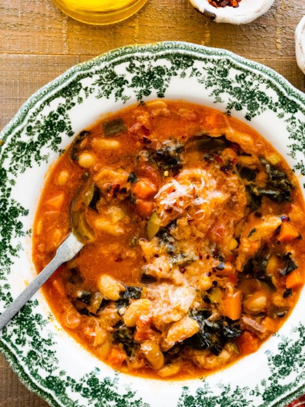 A warm bowl of the tuscan ribollita soup in an old fashioned bowl. Extra freshly grated parm on top for garnish. A spoon in the bowl.