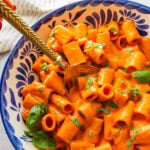 Roasted red pepper pasta in a bowl topped with basil with a spoon resting in it.