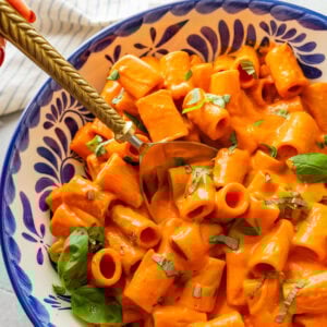 Roasted red pepper pasta in a bowl topped with basil with a spoon resting in it.