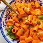 Roasted red pepper pasta in a bowl topped with basil with a spoon resting in it.