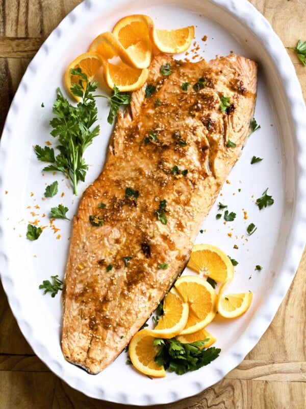 Baked honey orange sesame salmon on a white platter with orange slices.
