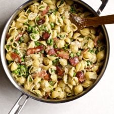 Creamy pasta shells with petite peas and bacon in a skillet pan