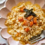 A bowl of butternut squash risotto garnished with sage and squash cubes, with a fork resting inside.