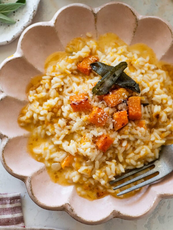 A bowl of butternut squash risotto garnished with sage and squash cubes, with a fork resting inside.