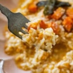 A bowl of butternut squash risotto garnished with sage and squash cubes, with a fork raising up one bite.