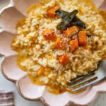 A bowl of butternut squash risotto garnished with sage and squash cubes, with a fork resting inside.