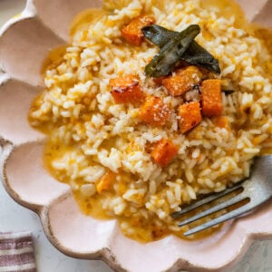 A bowl of butternut squash risotto garnished with sage and squash cubes, with a fork resting inside.