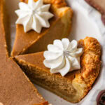 Two slices of pumpkin pie topped with whipped cream, separated from the rest of the pie in the pie dish.