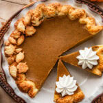 Two slices of pumpkin pie topped with whipped cream, separated from the rest of the pie in the pie dish.