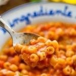 A bowl of pasta e ceci with a spoon holding a bite and more ingredients nearby.