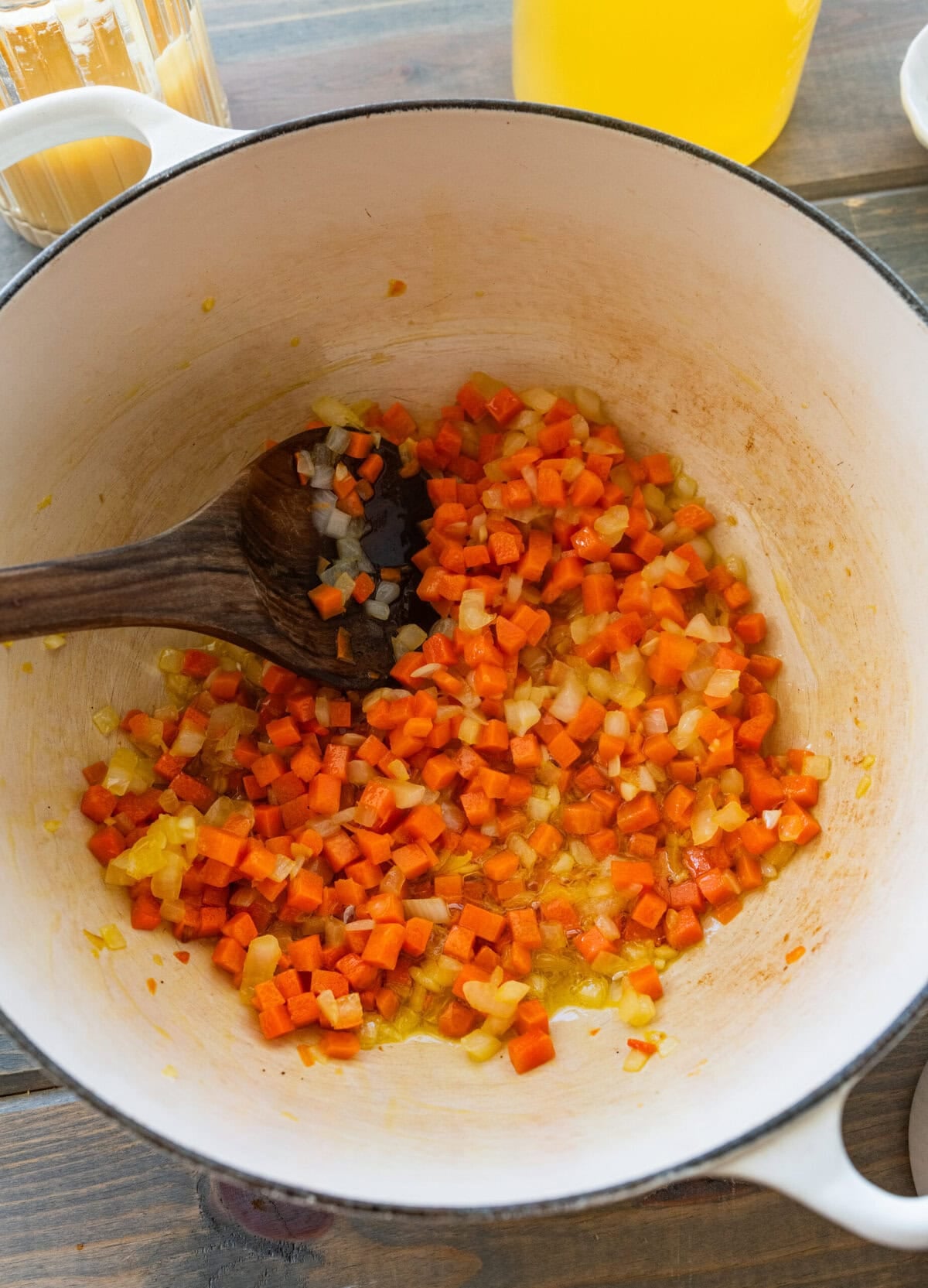 Carrots, onion, and garlic in a large pot being stirred by a wooden spoon.