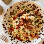 A bowl of peas and bacon pasta with a fork and more ingredients nearby.