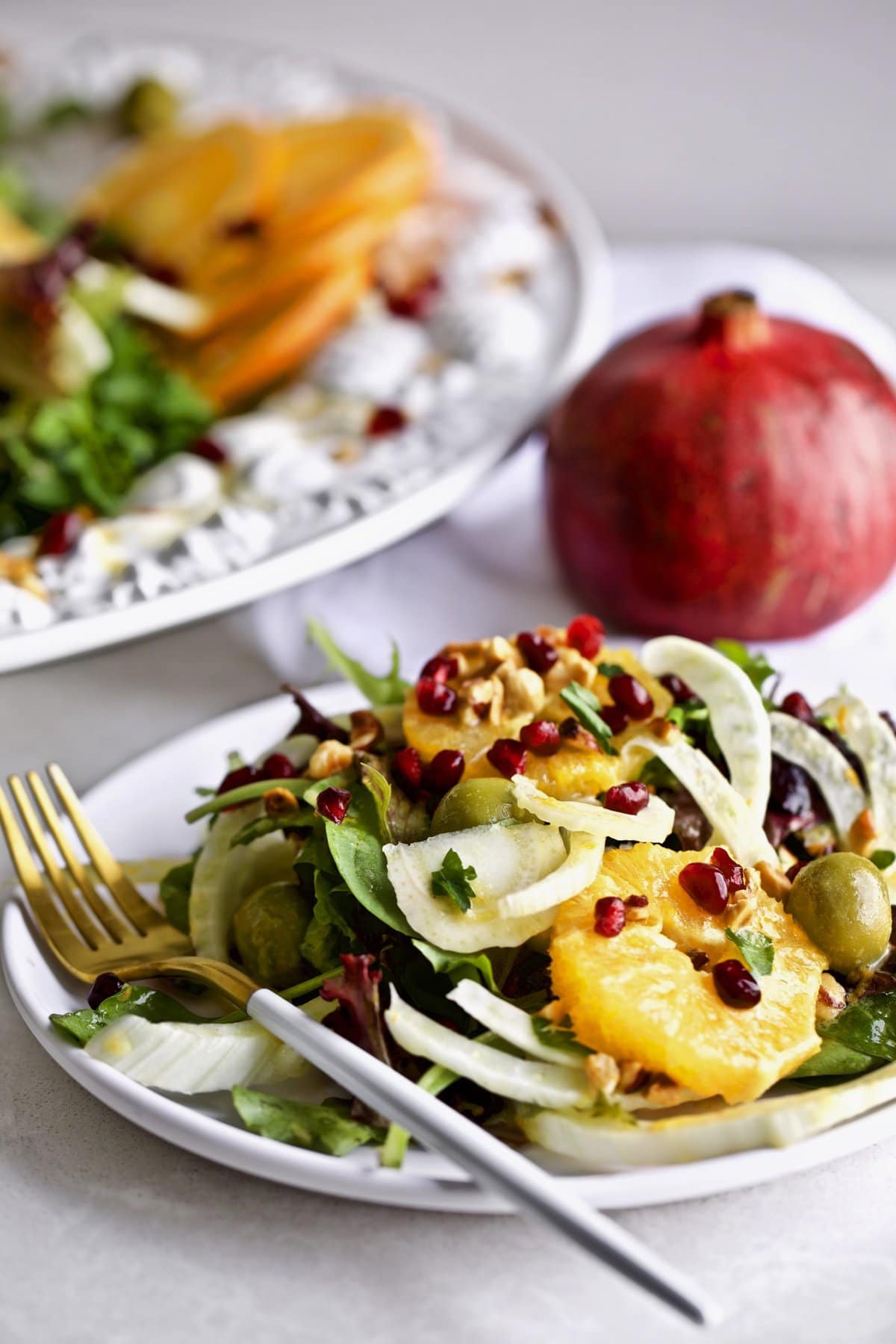 Orange and Fennel Salad Recipe on a plate with a pomegranate in the background.