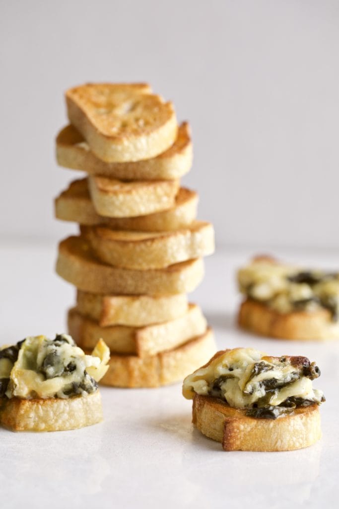 Stack of bread behind bread topped with artichoke spinach dip.