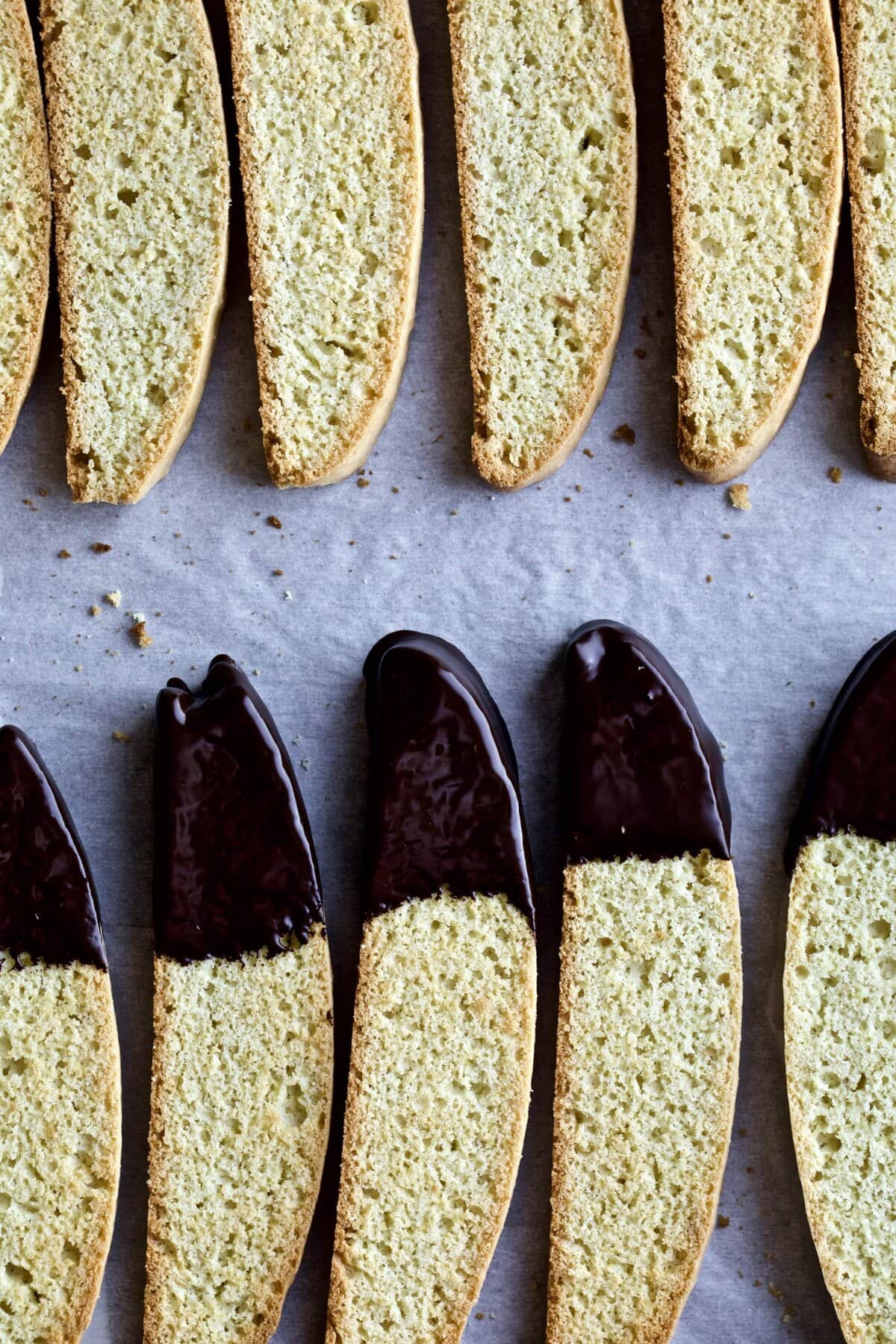 Italian biscotti cookies on a tray with half of them dipped in chocolate on one end.