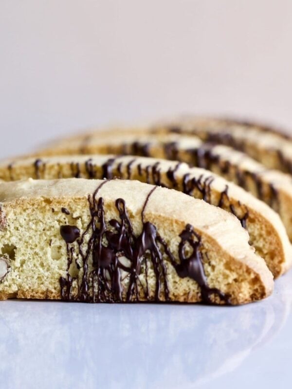 Italian almond biscotti on a white surface drizzled with chocolate.