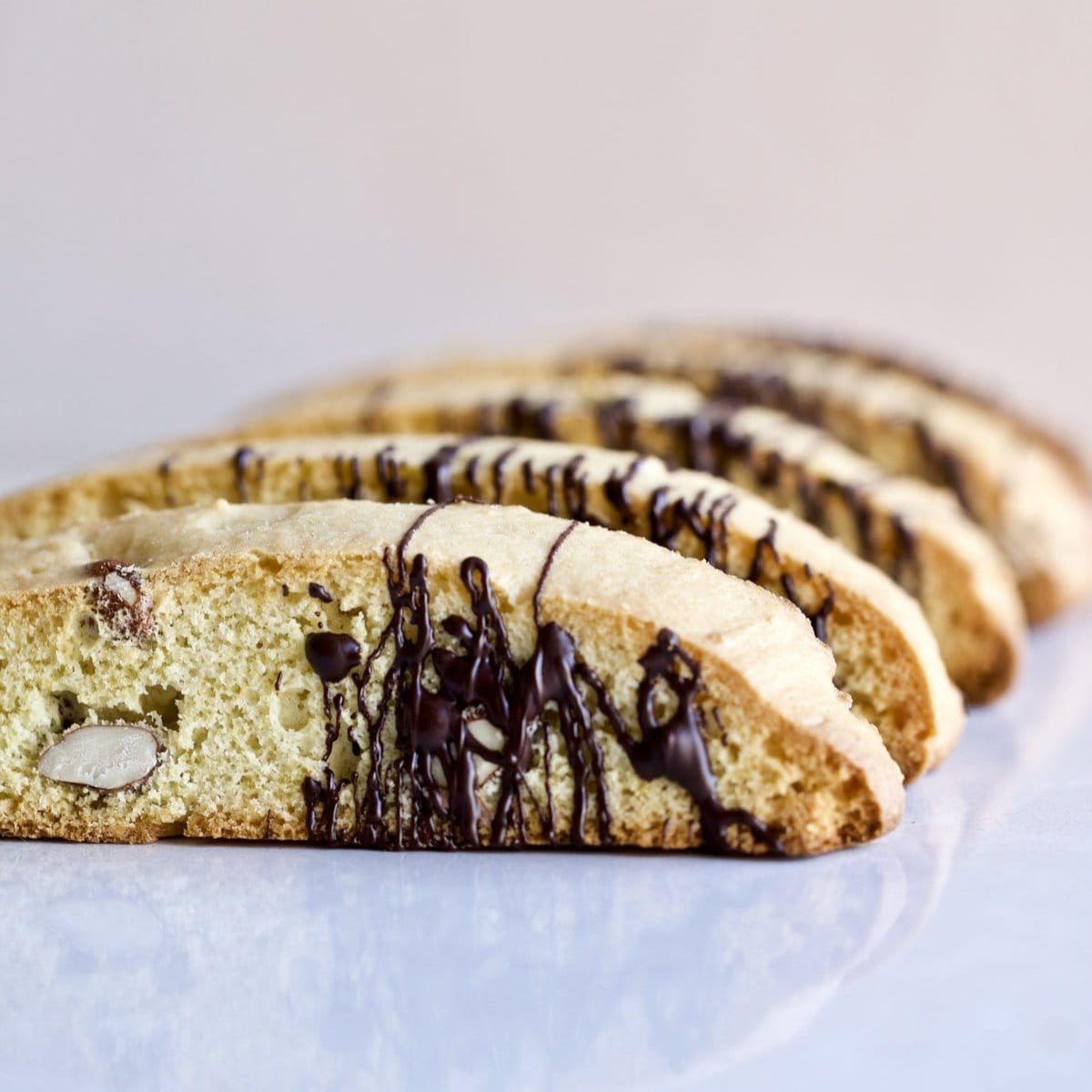 Italian almond biscotti on a white surface drizzled with chocolate.