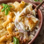 Ham and noodle casserole in a baking dish garnished with basil, and a scoop being taken out.