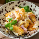 A bowl of ham and noodle casserole with a fork resting inside.