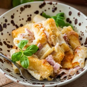 A bowl of ham and noodle casserole with a fork resting inside.