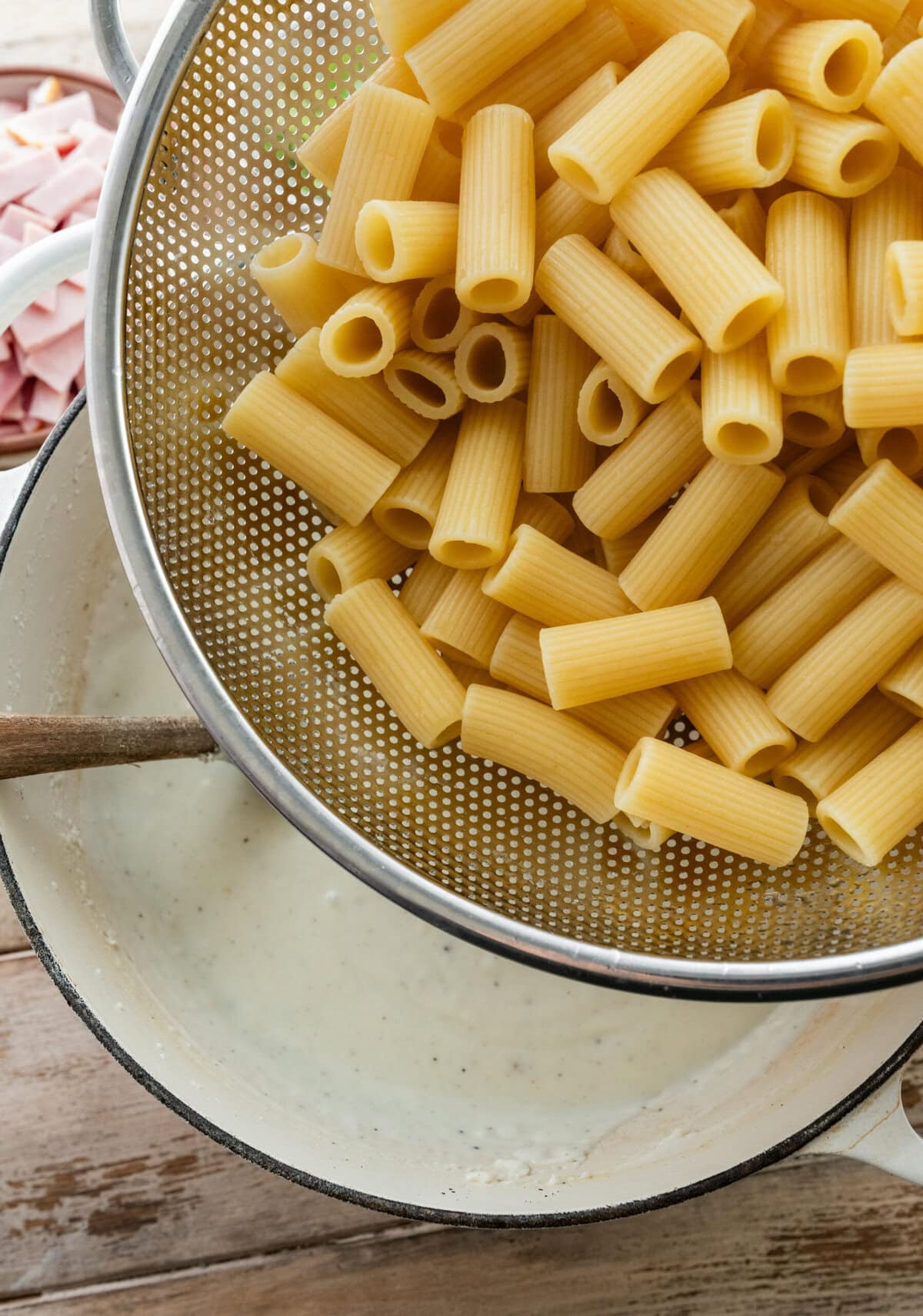 Cooked pasta in a strainer being poured into the bechamel sauce.