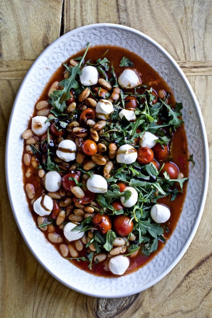 Warm white bean arugula salad with mozzarella and a balsamic glaze in a large serving platter.