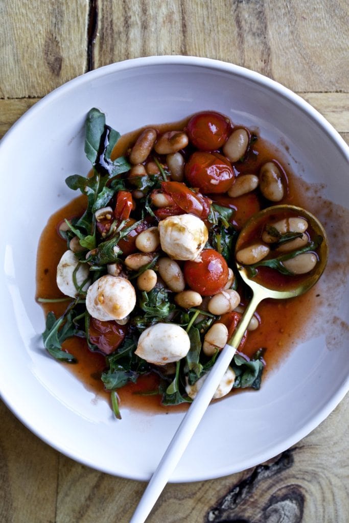 Spoon with a scoop of warm white bean salad with arugula and mozzarella.