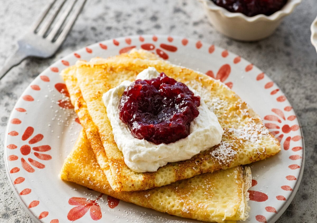 folded up swedish pancakes on a plate with toppings.