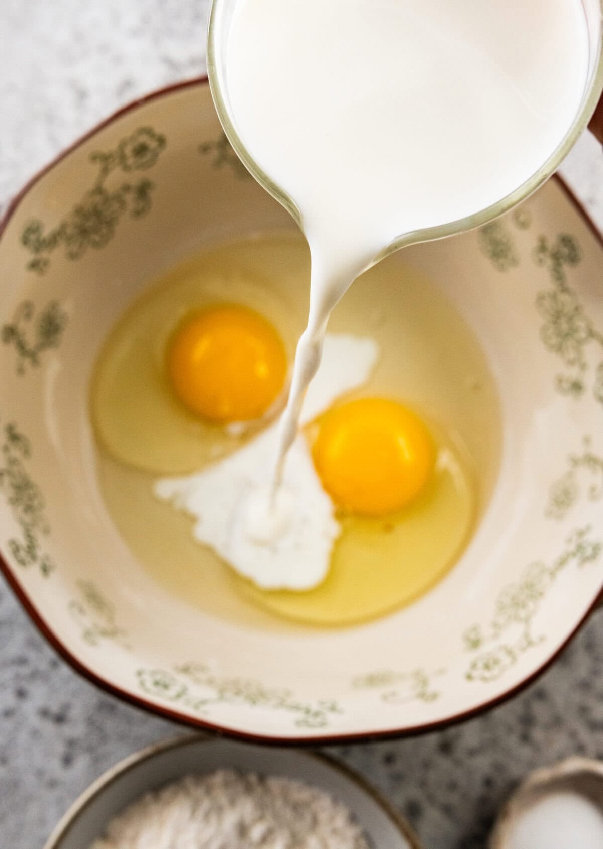 milk being poured into the mixing bowl that contains eggs.