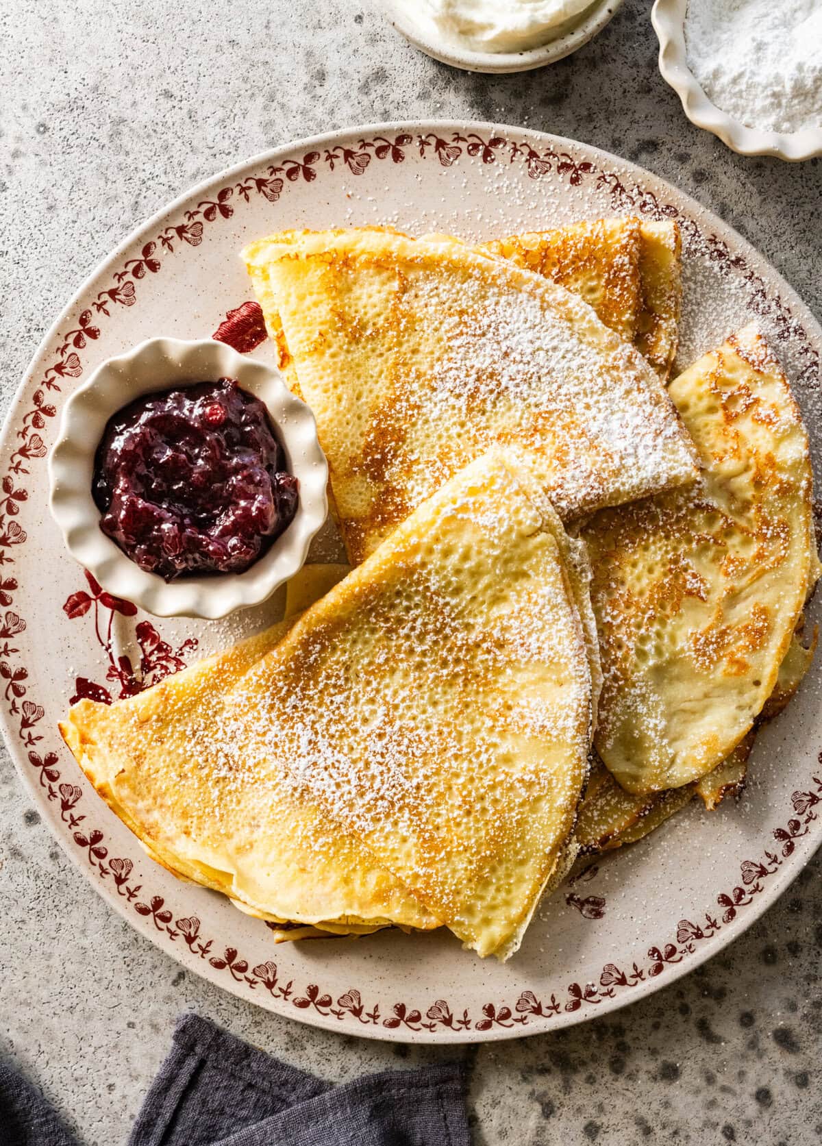 folded up swedish pancakes on a plate with a bowl of preserves.