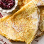 folded up swedish pancakes on a plate with a bowl of preserves.