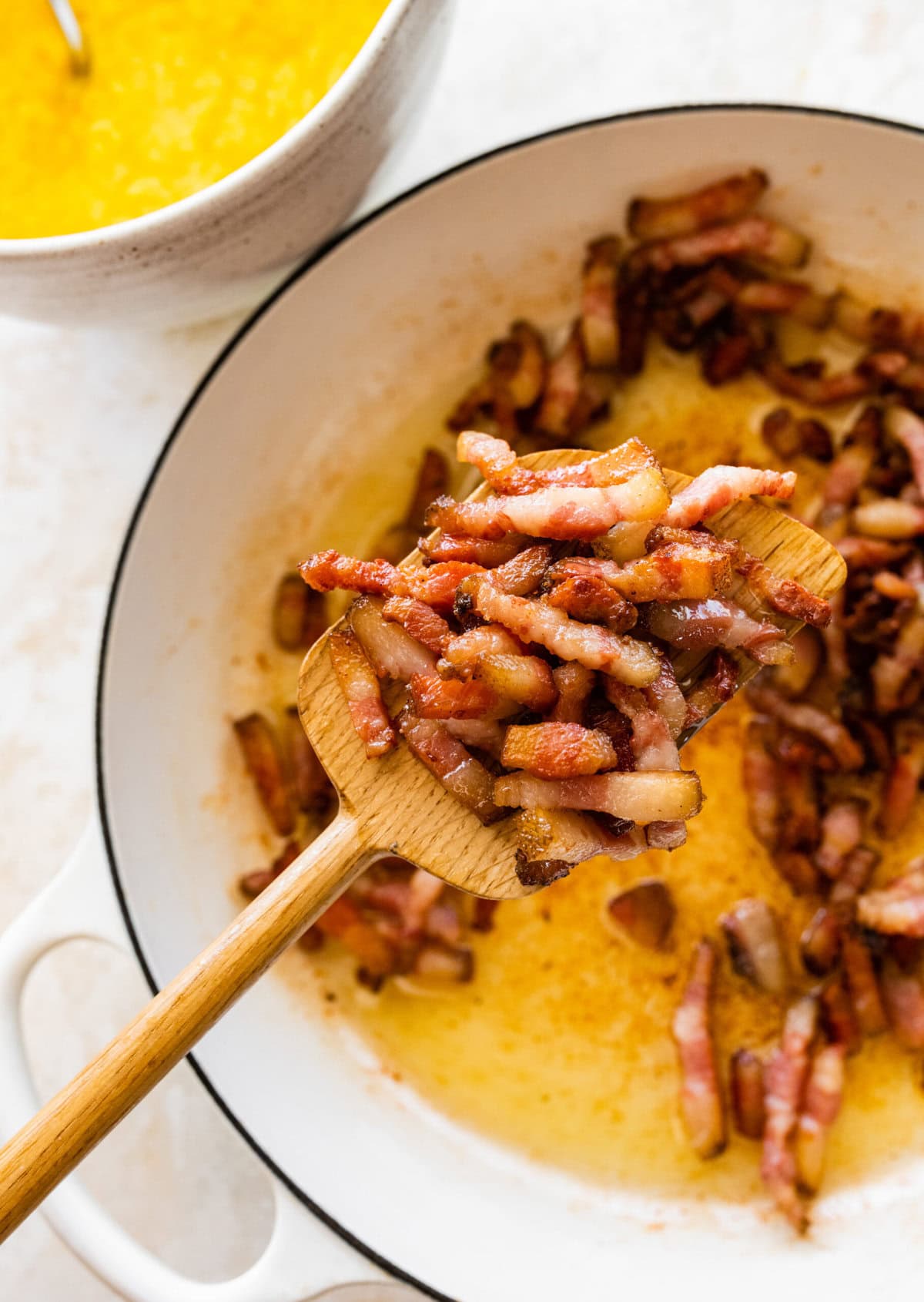 A spoon holding up a bit of the cooked guanciale over the skillet.