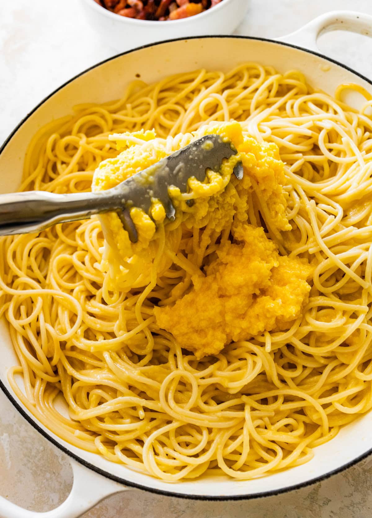 Adding the egg and parmesan mixture to a skillet of hot spaghetti.