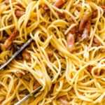 Spaghetti mixed with carbonara sauce in a skillet.
