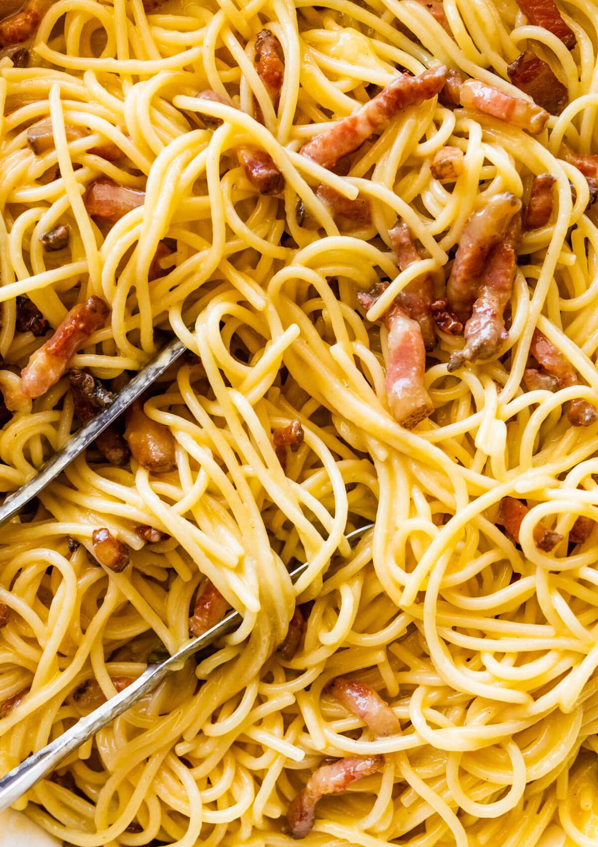 Spaghetti mixed with carbonara sauce in a skillet.