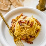 A plate of traditional carbonara on a plate with a gold fork to the side.