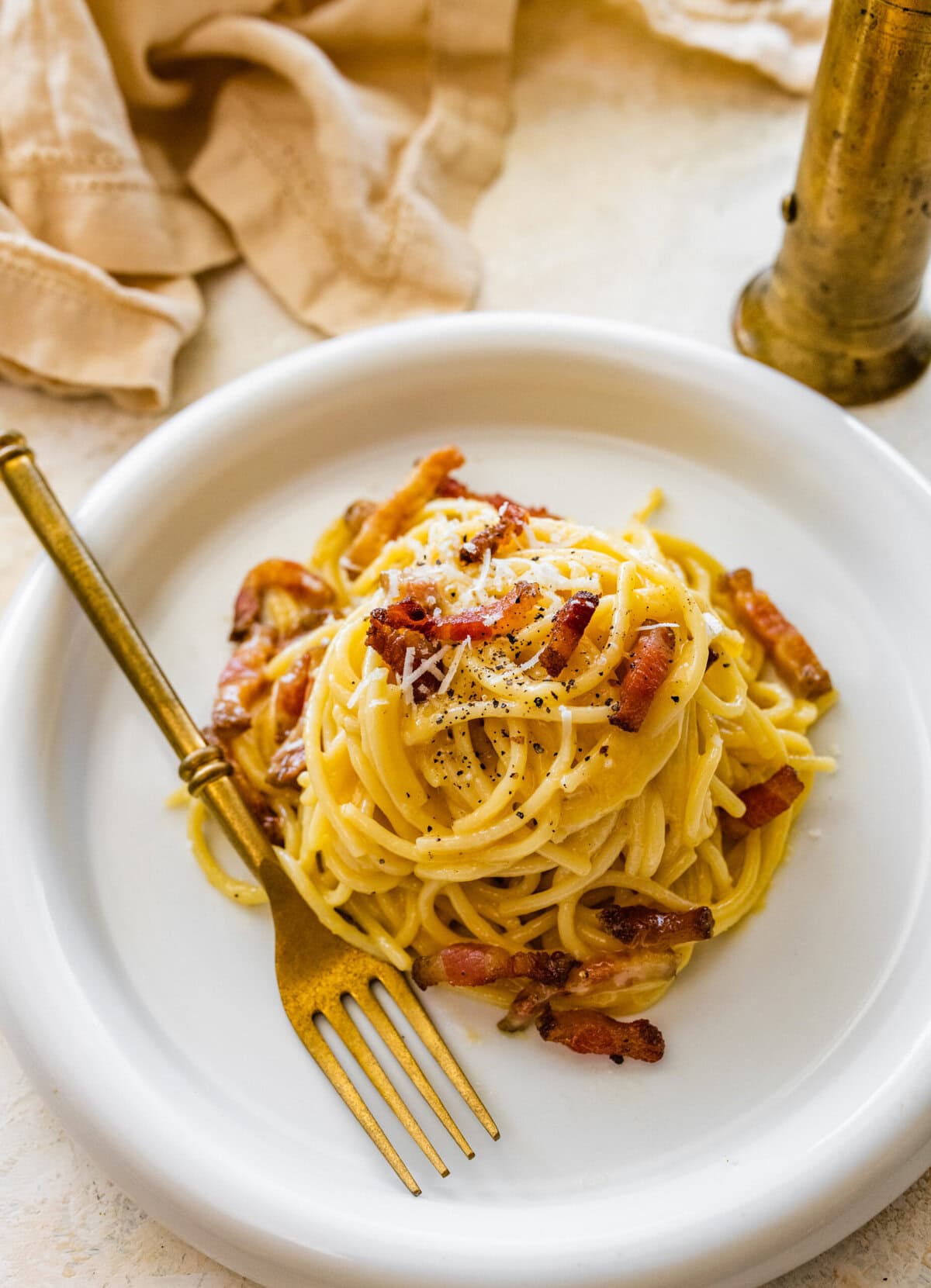 A plate of traditional carbonara on a plate with a gold fork to the side.