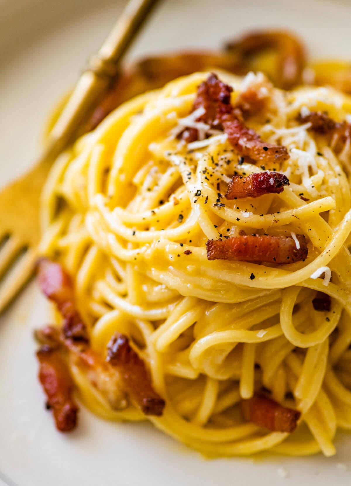 Carbonara pasta on a white plate with shreds of parmesan and pieces of meat on top.
