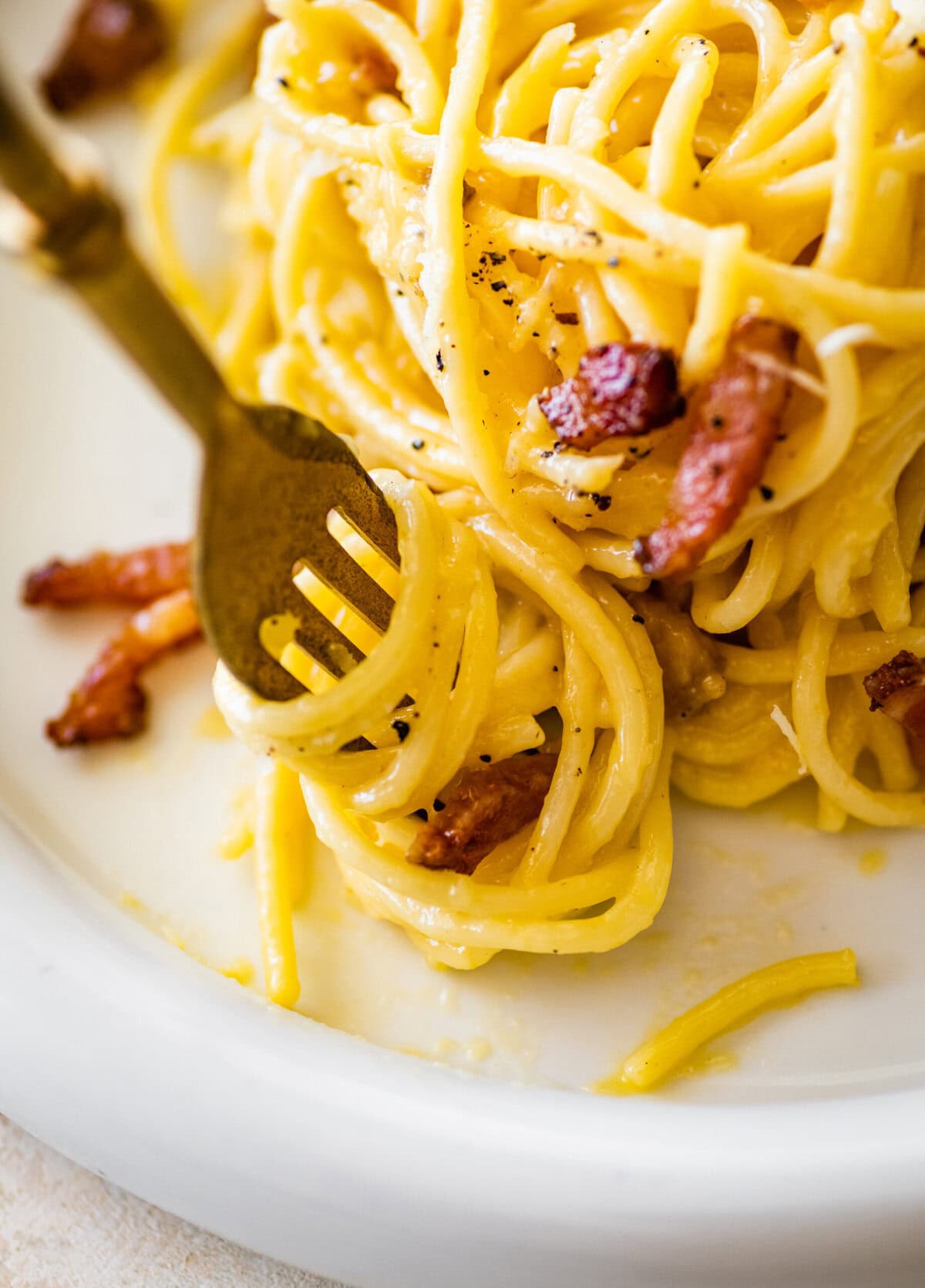 A fork twirling up a bite of pasta next to the serving of plated carbonara.