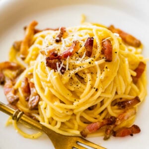 Carbonara pasta on a plate with bits of guanciale and shredded parmesan cheese on top.