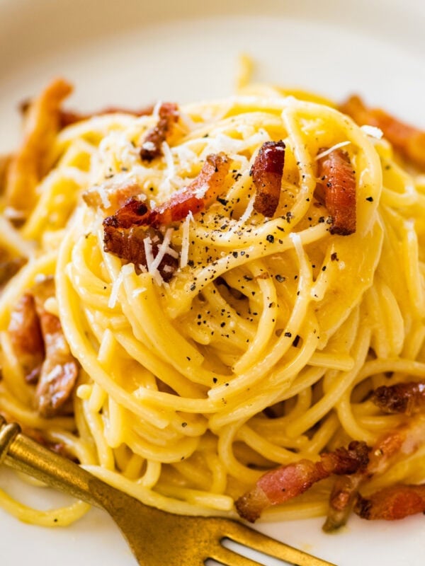 Carbonara pasta on a plate with bits of guanciale and shredded parmesan cheese on top.