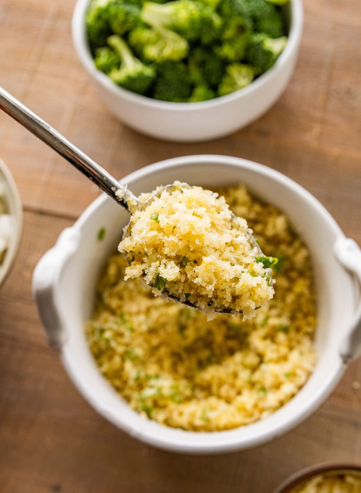 a spoonful of breadcrumbs held over a bowl of more breadcrumbs.