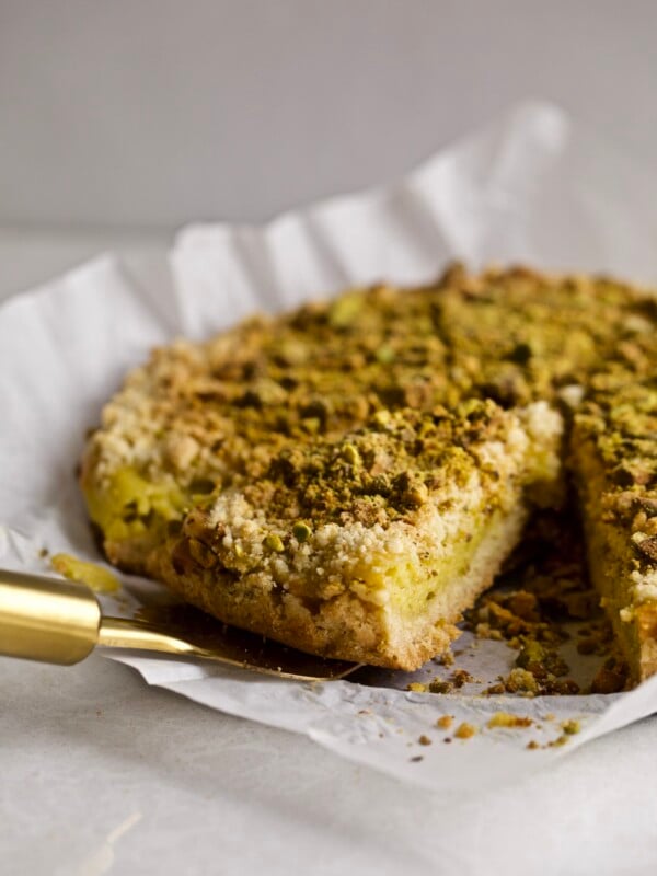 Italian Crumb Cake with Pistachio Cream (Sbriciolata) on a cake plate with a slice taken out with a pie server. Side angle shot.