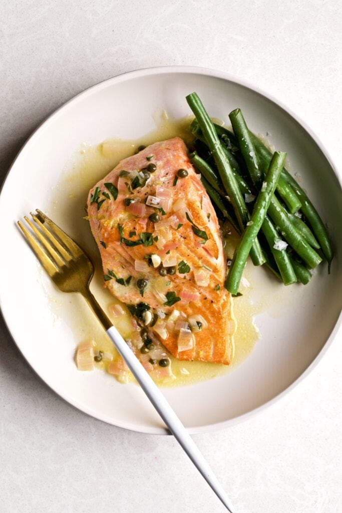 Salmon in Lemon Butter Caper Sauce, salmon piccata, garnish, green beans on a white plate with fork.