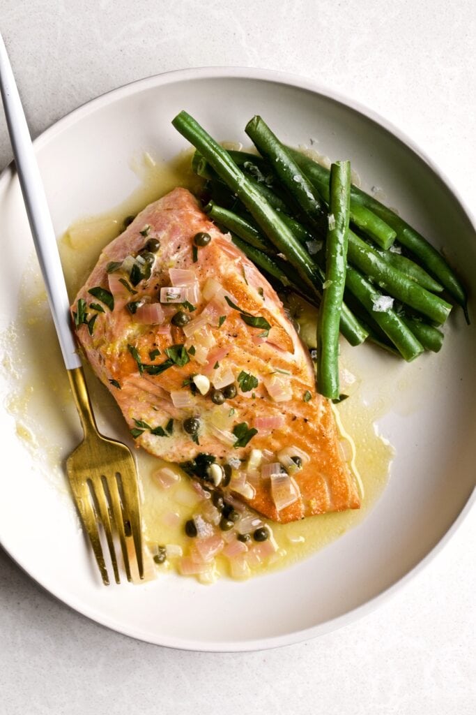 Salmon Piccata with lemon sauce and green beans on a plate with a fork.