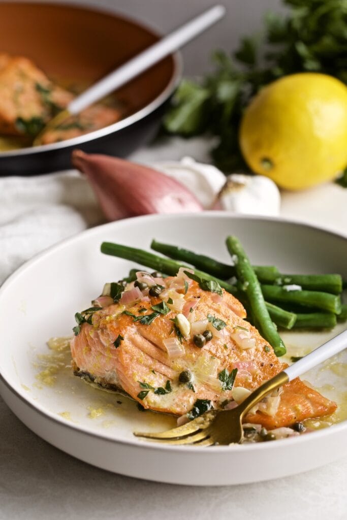 Salmon Piccata with green beans on a plate with a fork.
